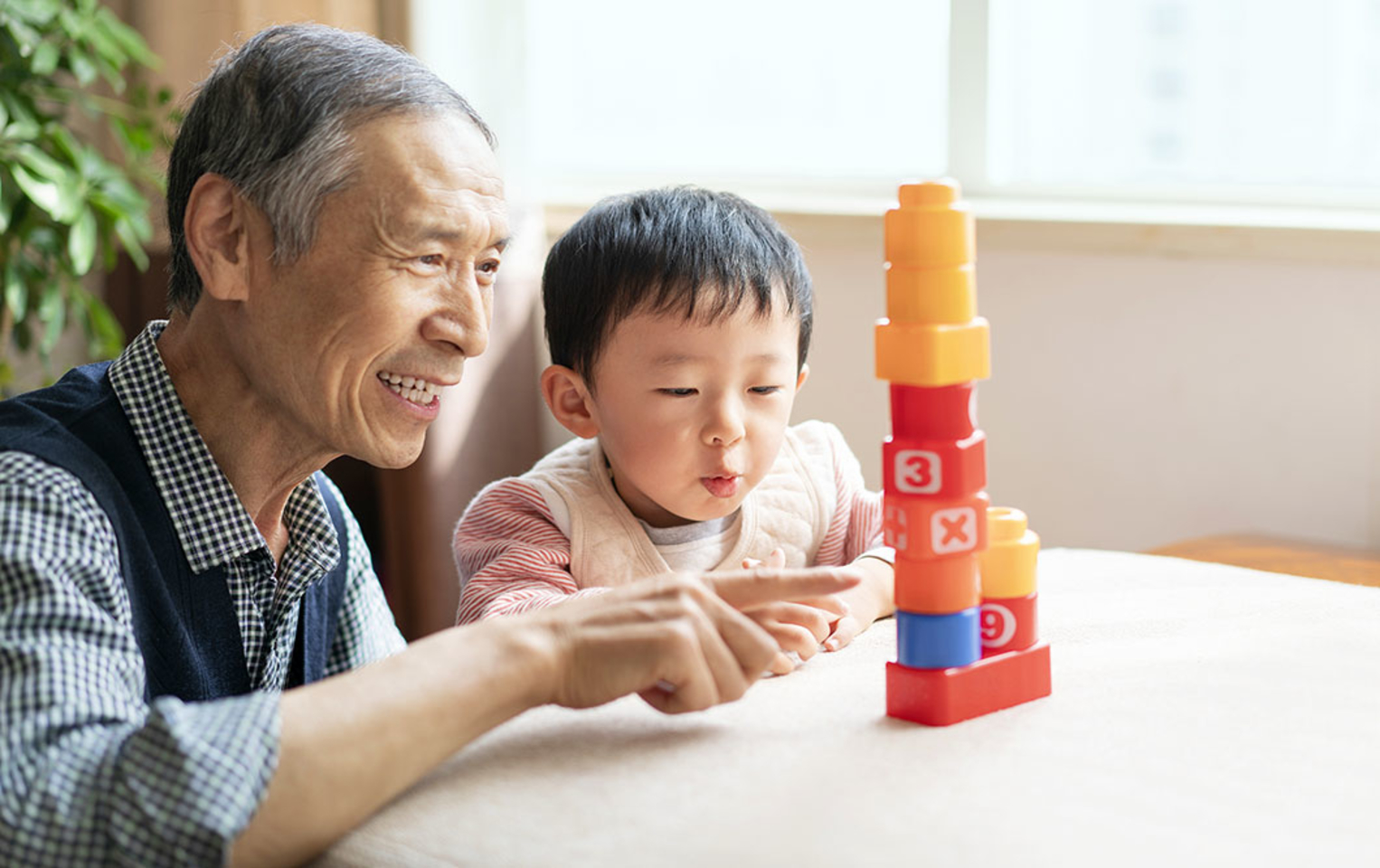 Grandfather and grandchild sitting at a table and playing with blocks