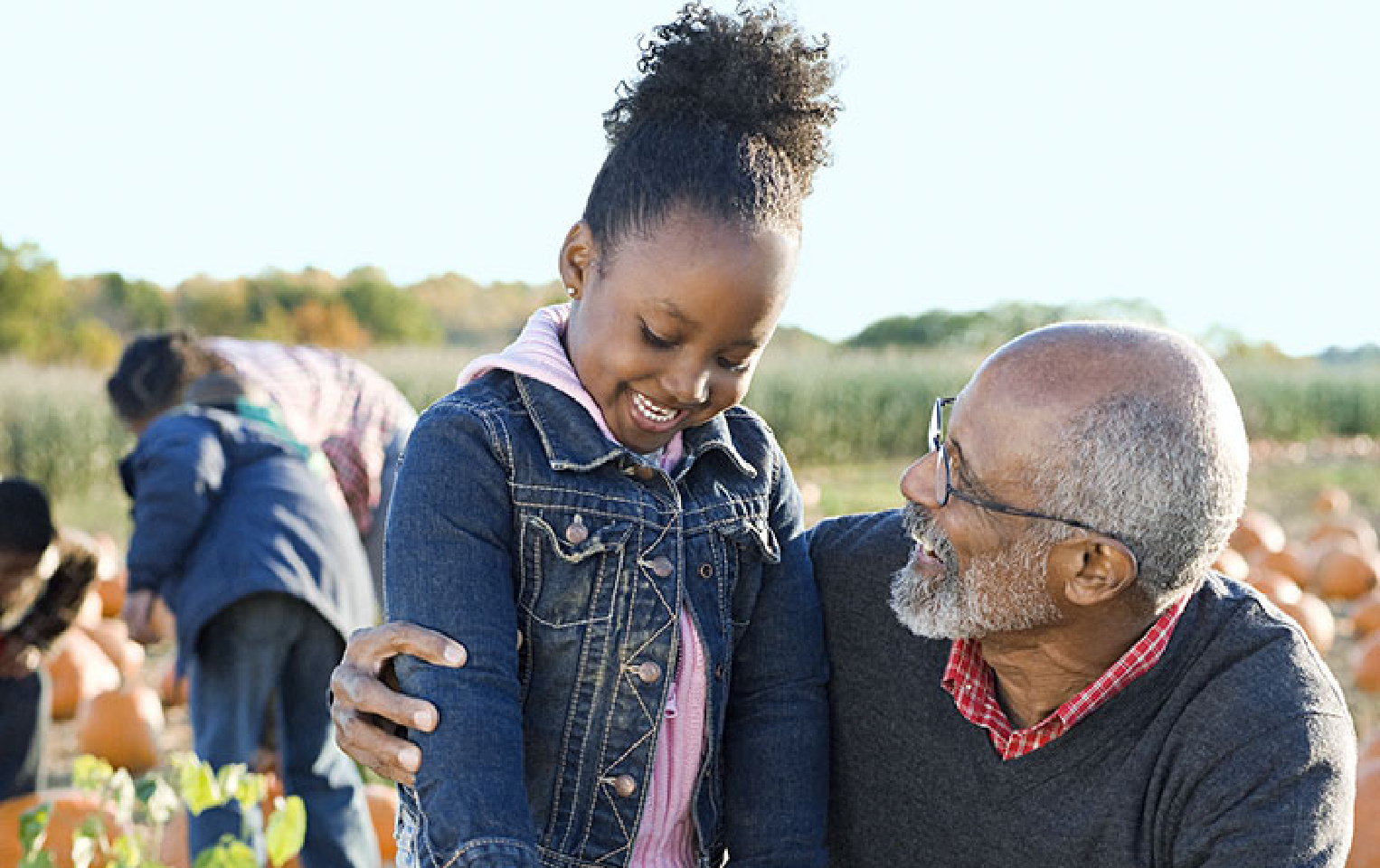 Grandfather and grandchild smiling at each other at a pumpkin patch