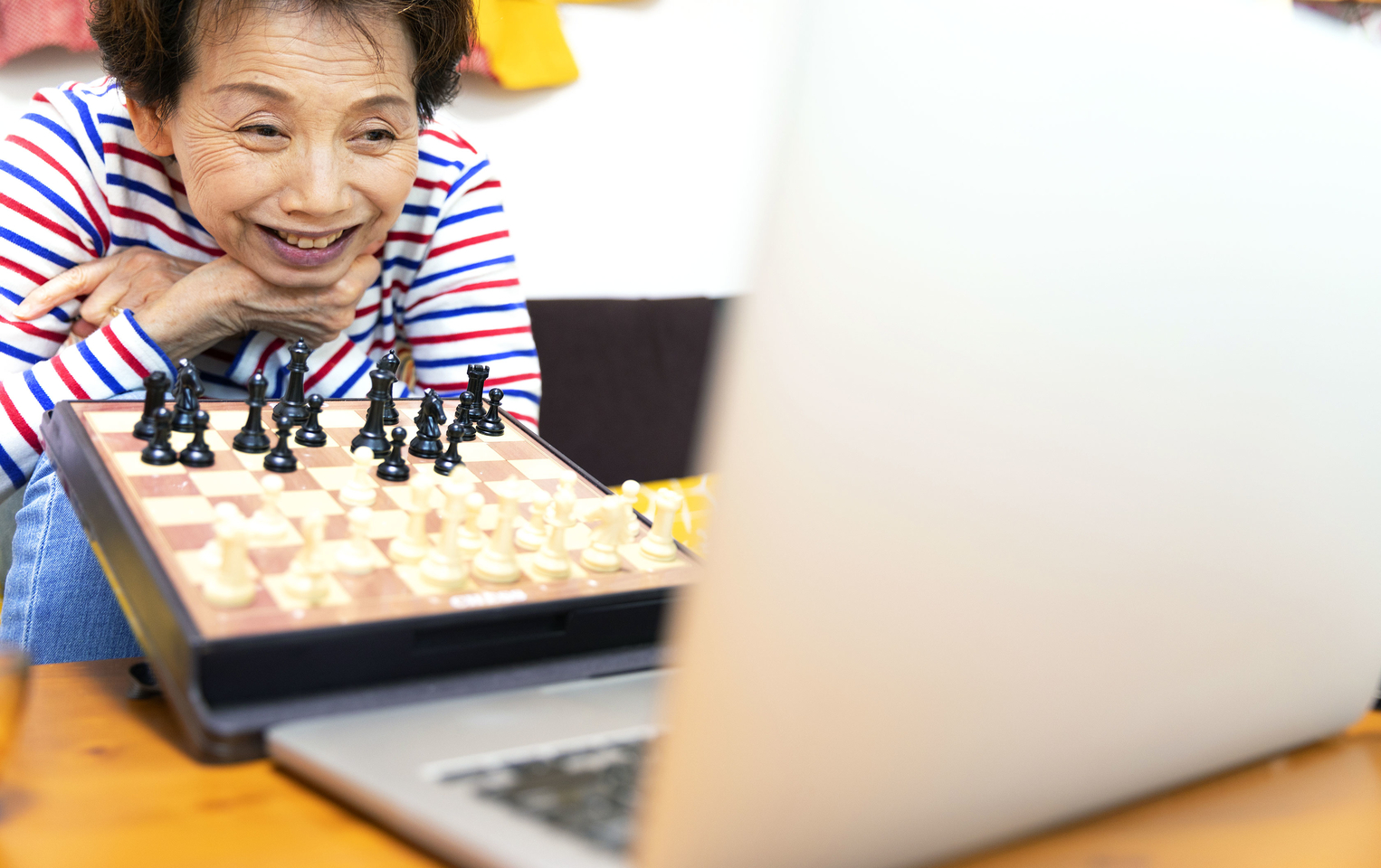 A woman in a blue, white and red shirt showing her chess board in front of a laptop