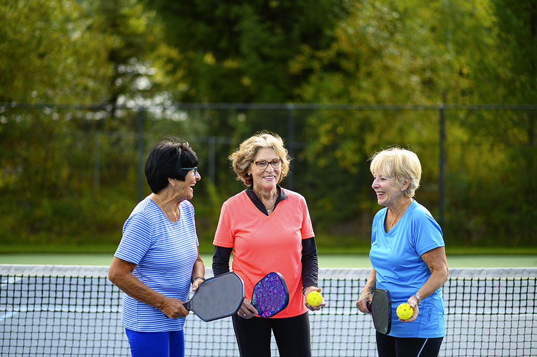 Three woman talking in a tennis court with their pickleball paddles and ball