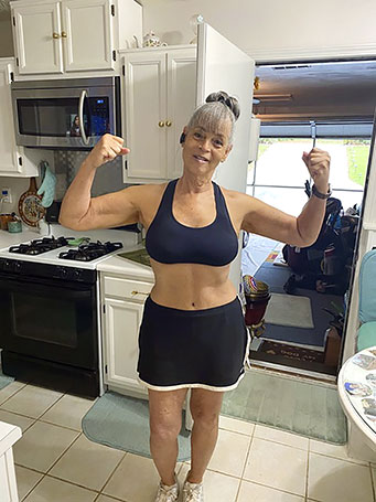 Cathy in a flexed pose wearing a black work out outfit.