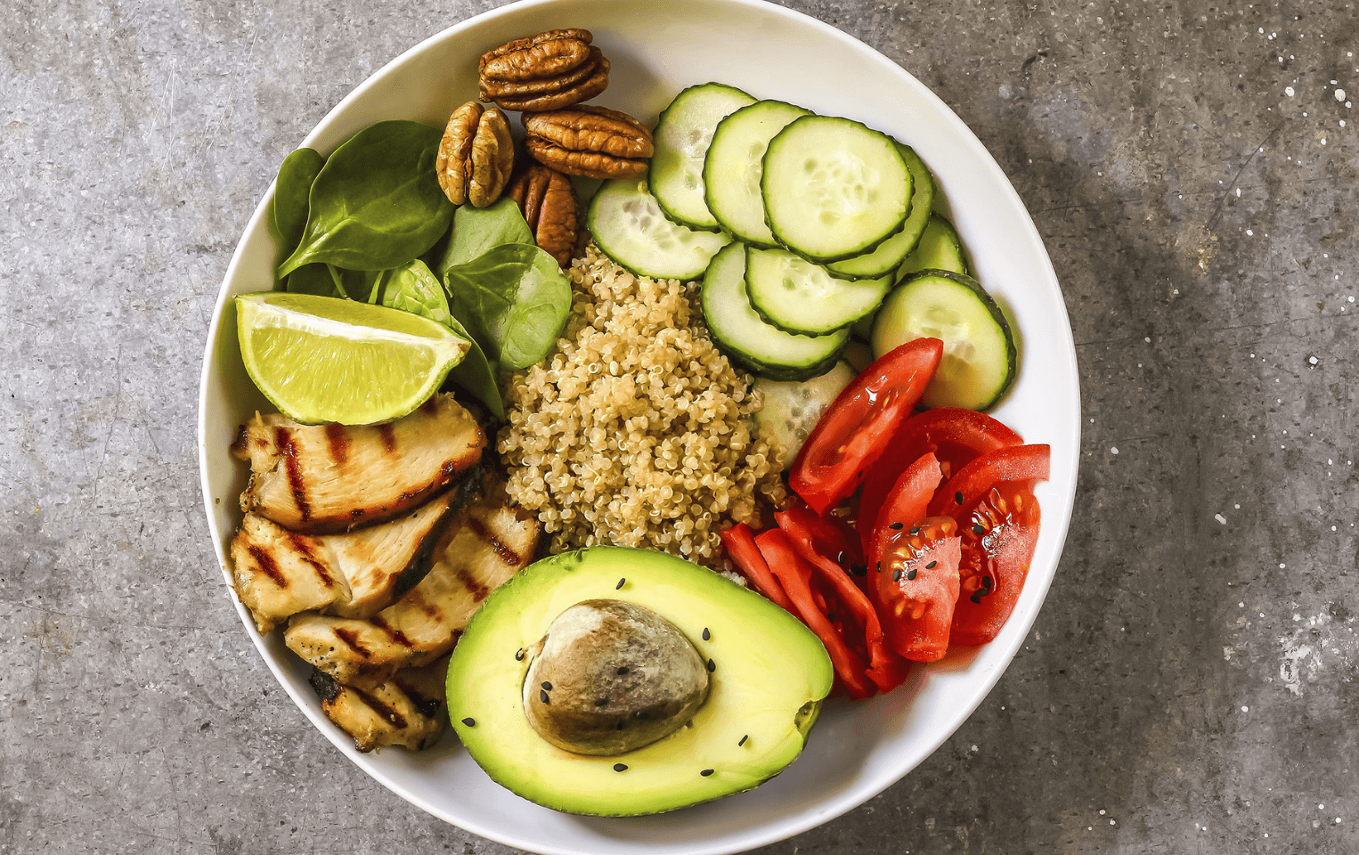Bowl of grilled chicken quinoa salad with avocado, cucumbers, and tomatoes.