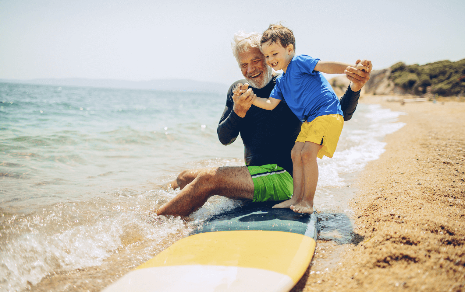 Grandfather teaching grandson how to surf on a beach.